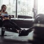 Jauna sportininkė sporto salėje naudojasi irklavimo treniruokliu