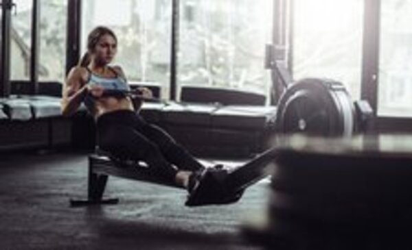 Jauna sportininkė sporto salėje naudojasi irklavimo treniruokliu